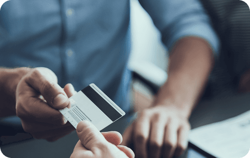 Persona entregando una tarjeta de crédito en la mano de otra persona con camisa de vestir