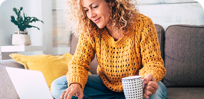 Mujer sentada en un sofá, escribiendo en la computadora y sosteniendo una taza